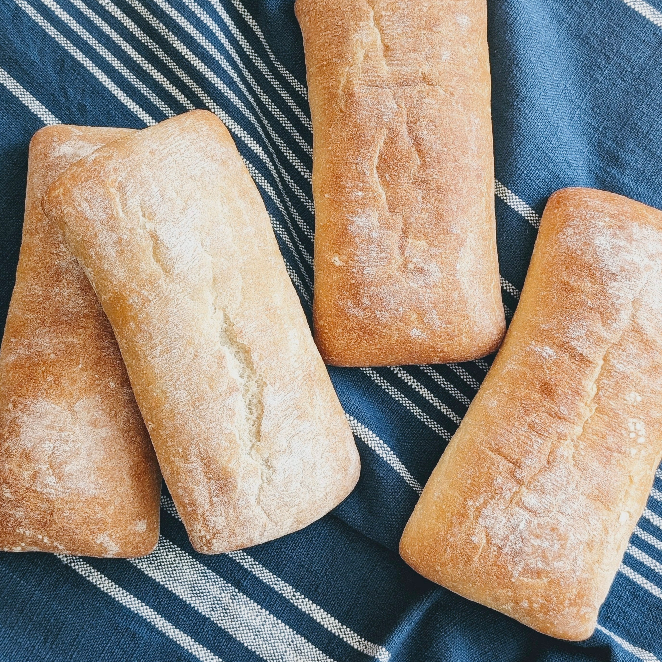 Four Slow-Fermented Ciabatta Sandwich Rolls on a blue striped cloth