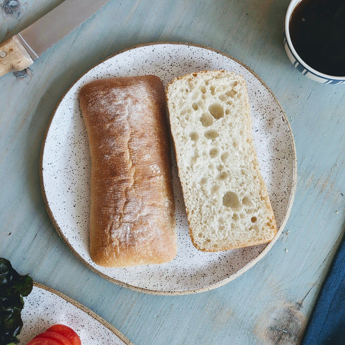A Slow-Fermented Ciabatta Sandwich Roll on a plate, with one roll sliced open to show the inside texture.