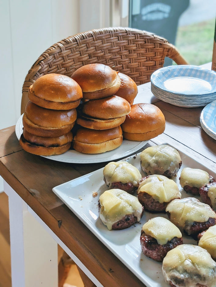 A stack of burger buns and a platter of cheeseburgers on a table