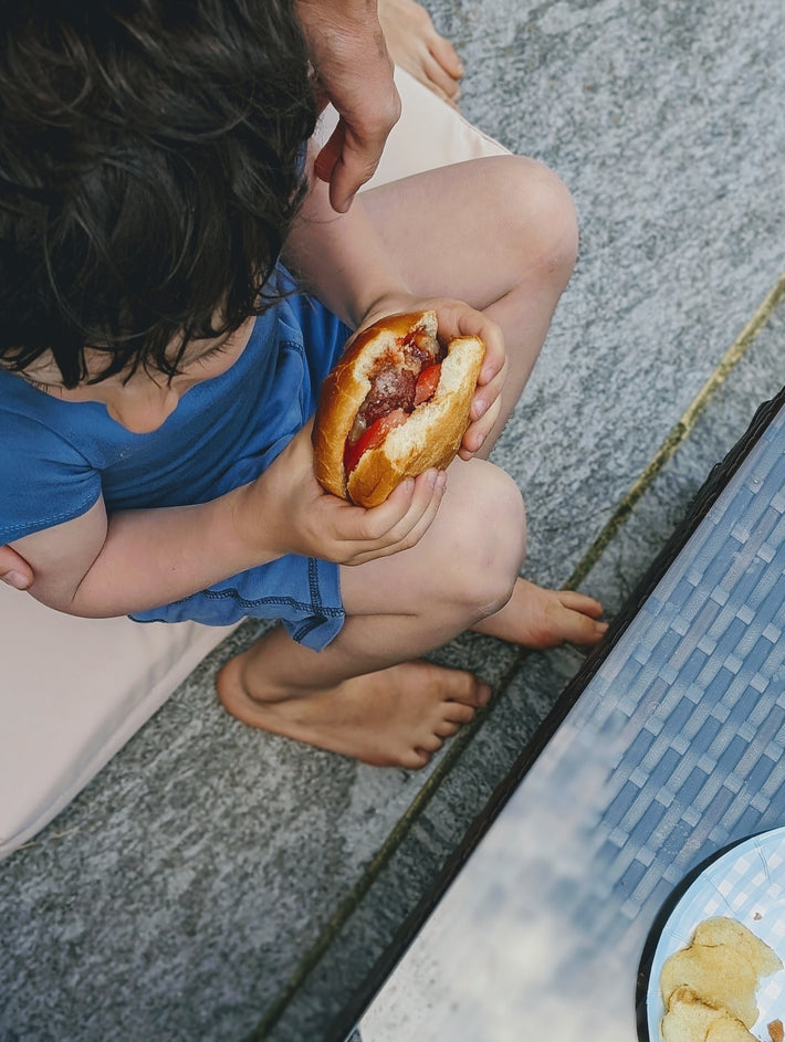 Child holding a hot dog in a bun, sitting on a patio