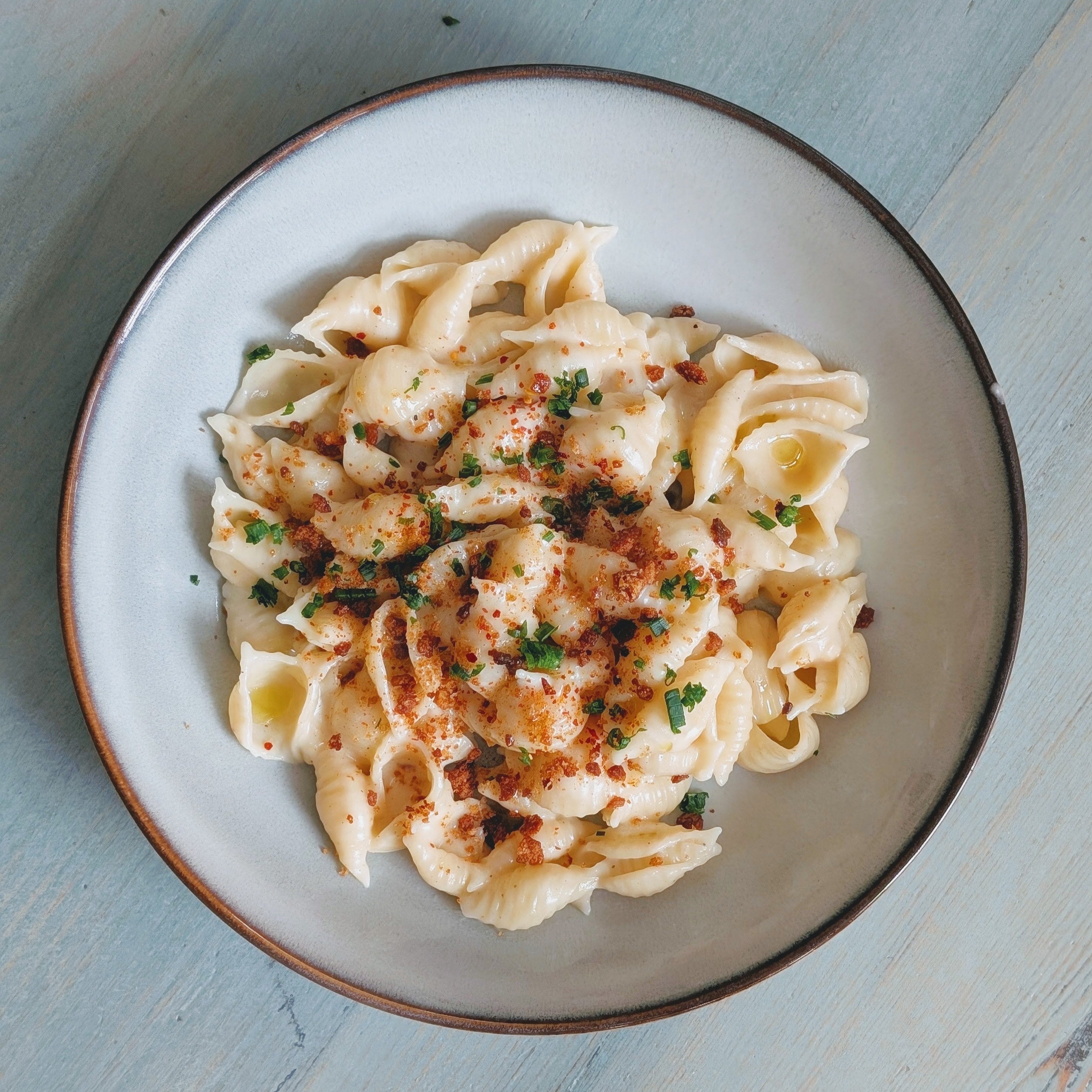 A bowl of gluten-free fresh shells pasta topped with herbs and seasoning.