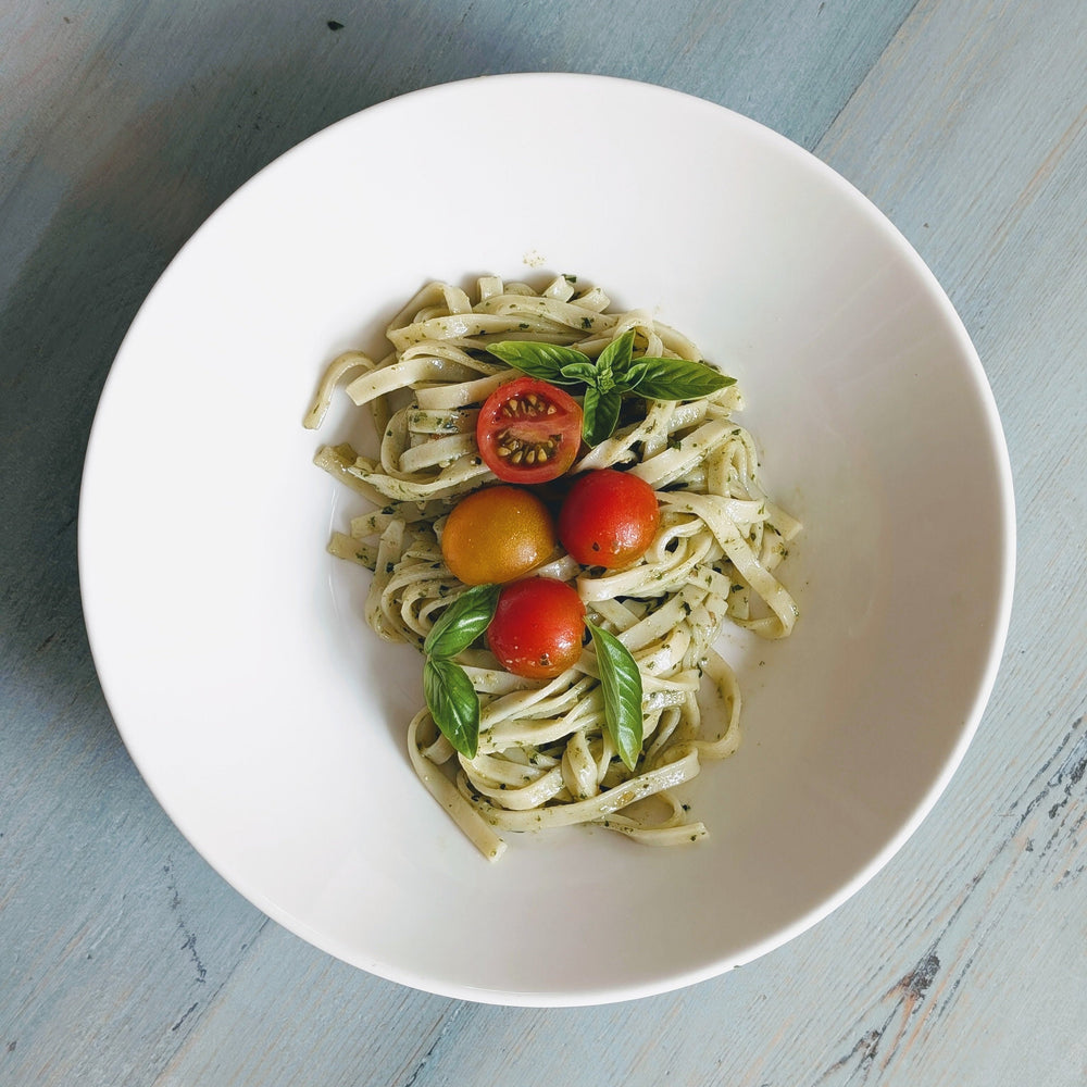 A bowl of gluten-free fresh linguine topped with cherry tomatoes and basil leaves.
