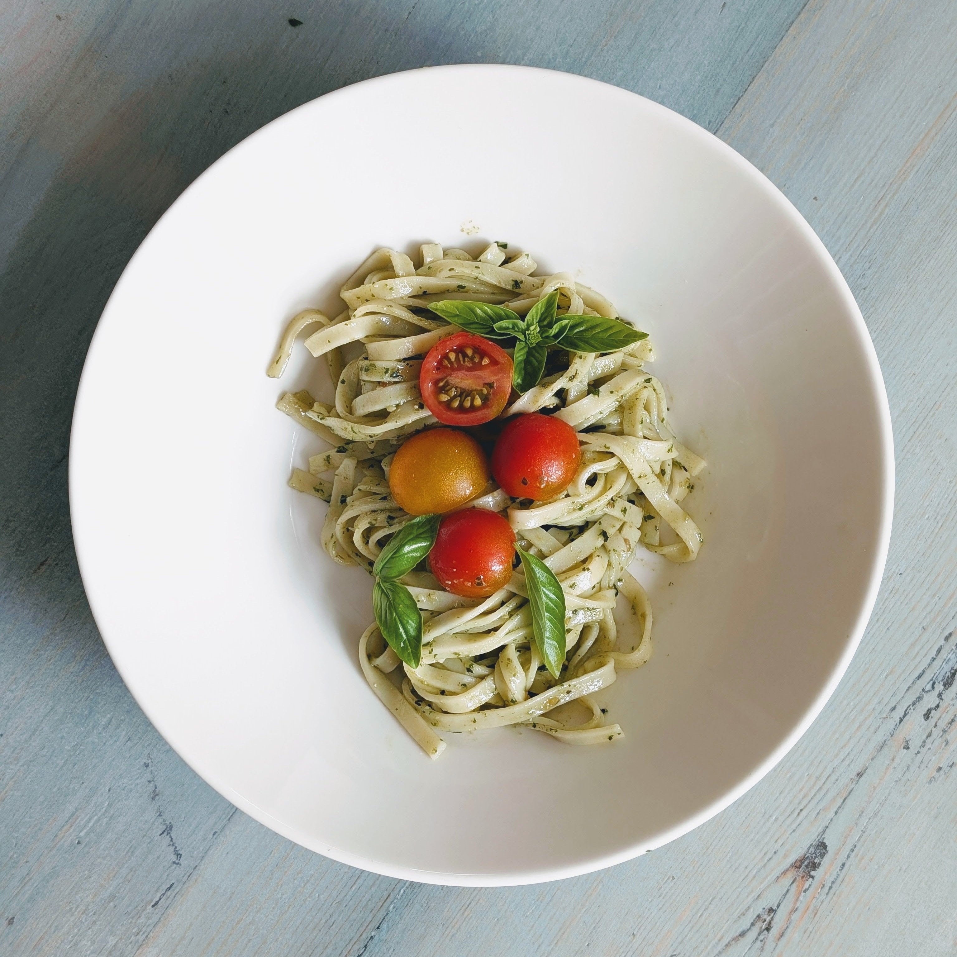 A bowl of gluten-free fresh linguine topped with cherry tomatoes and basil leaves.