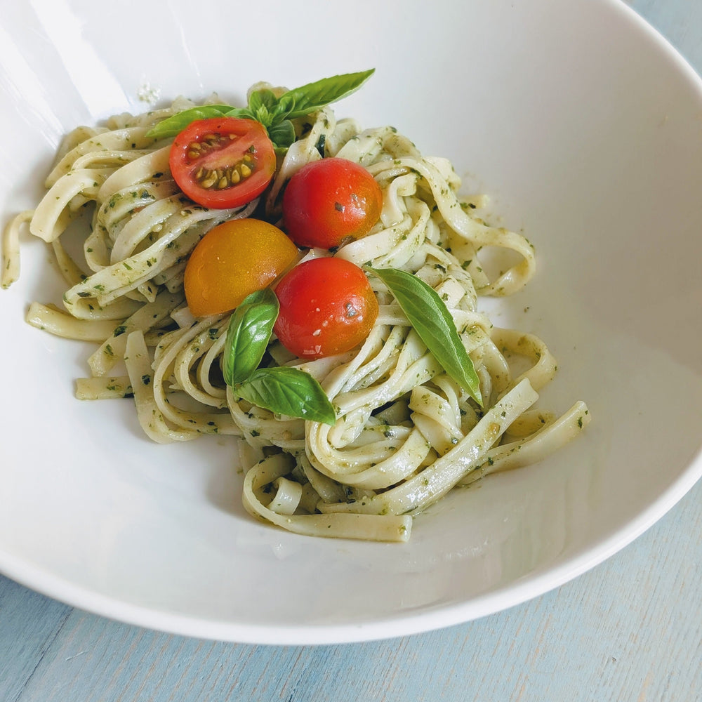 Fettuccine tossed in basil pesto with cherry tomatoes and basil leaves in a white shallow bowl.