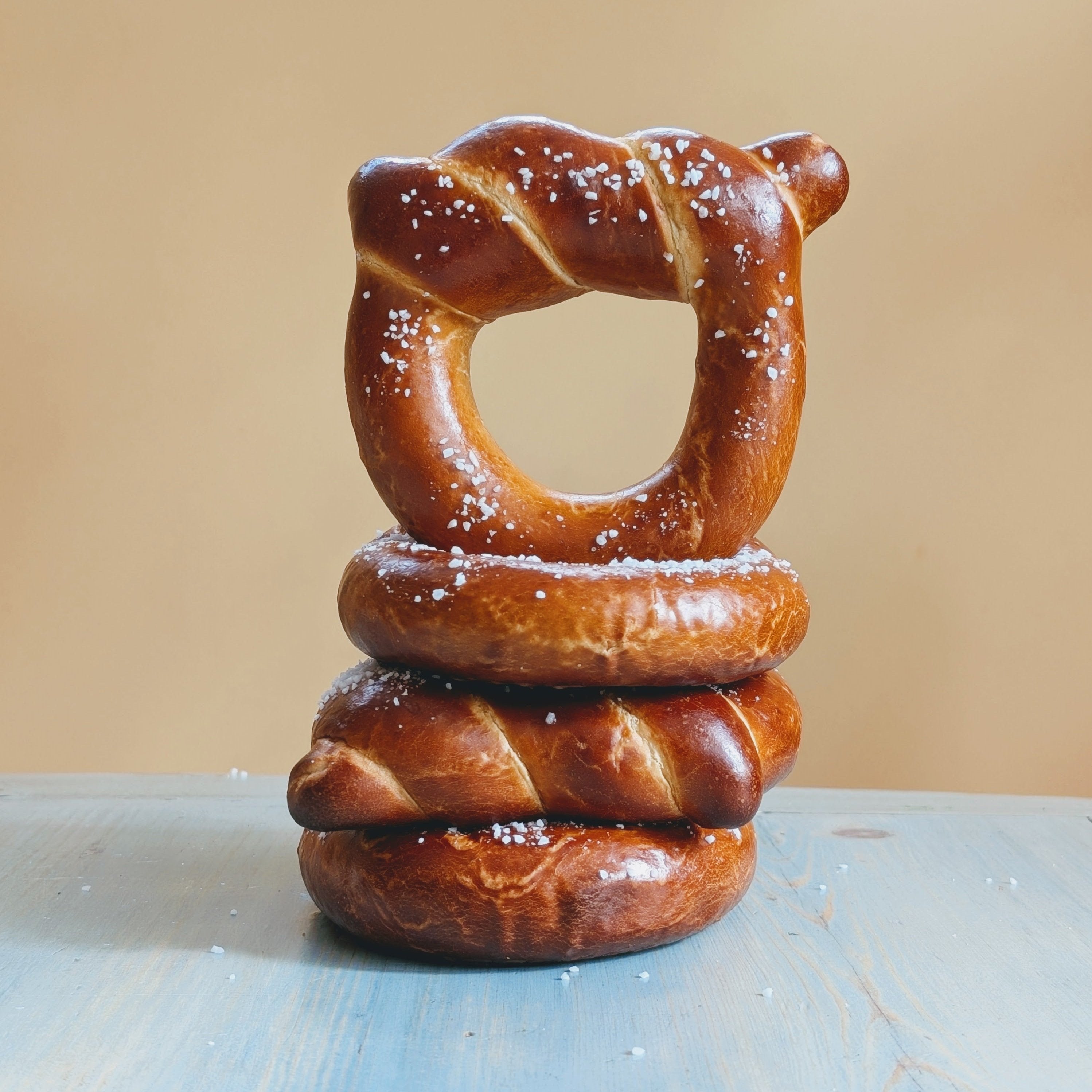 Three stacked soft pretzels sprinkled with coarse salt on a light blue table and beige background