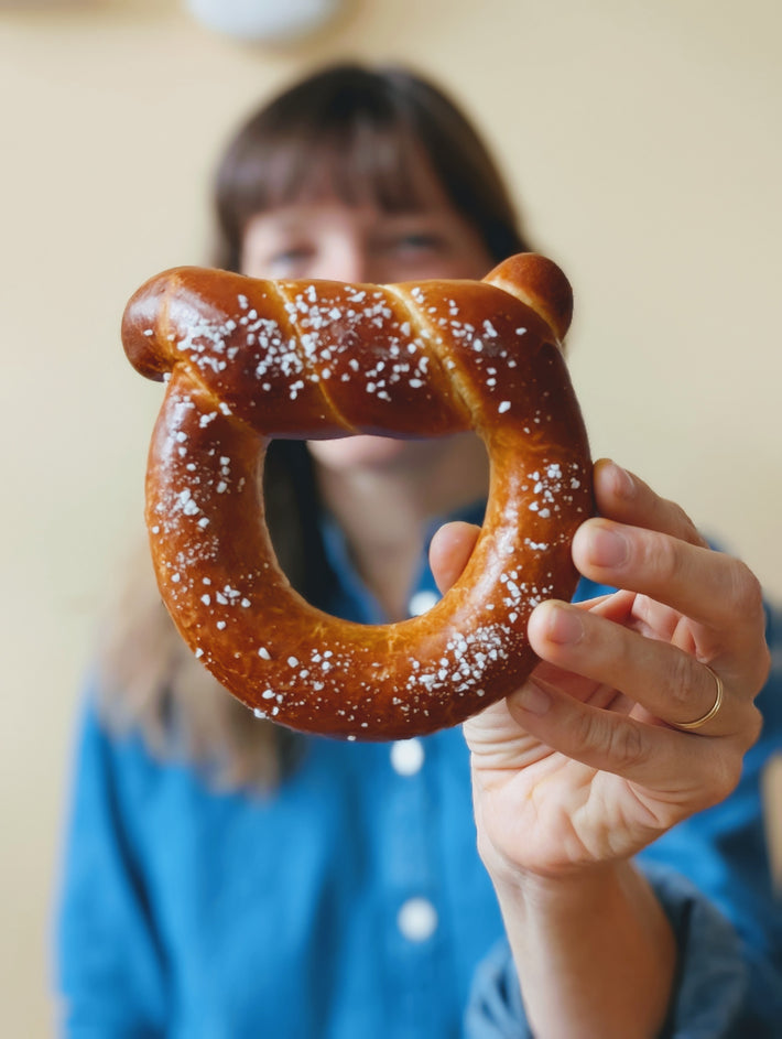 Artisanal Bavarian Pretzel held by a person, with salt on top.