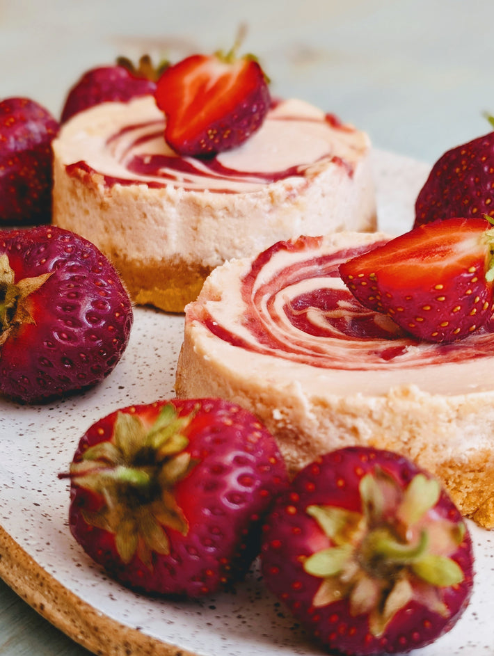 Mini strawberry-swirl cheesecakes on a speckled plate, garnished with halved fresh strawberries