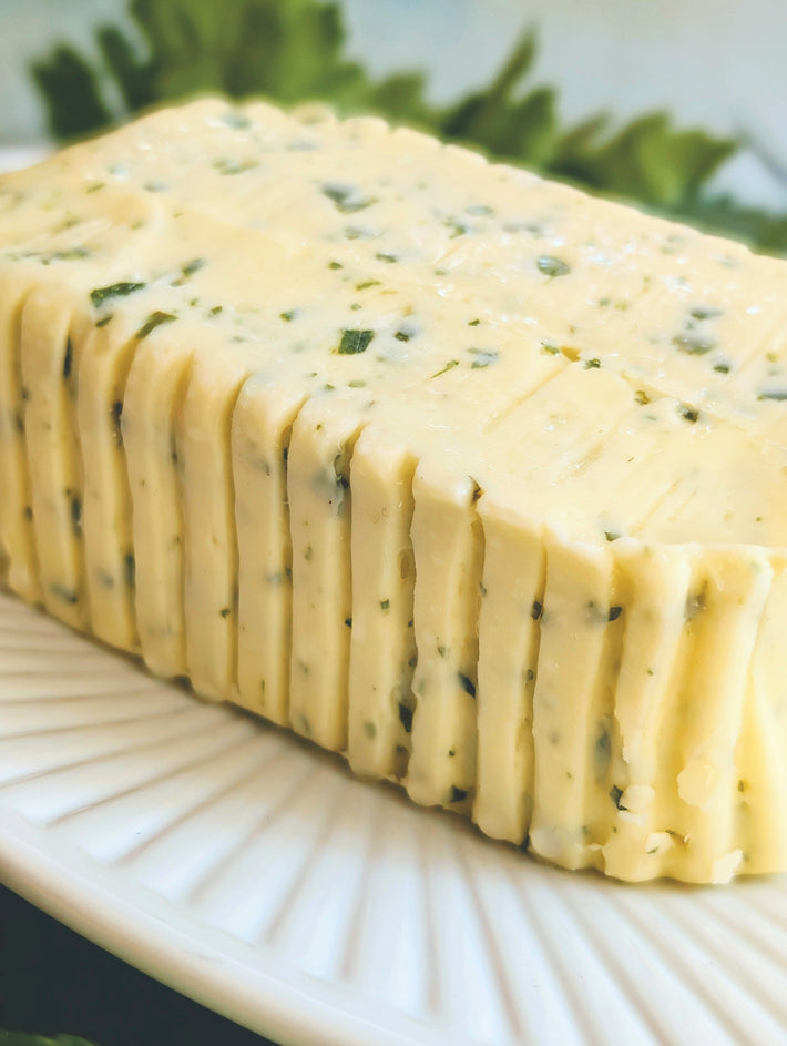 Rolled log of herb-speckled butter sliced into ridged rounds on a white plate