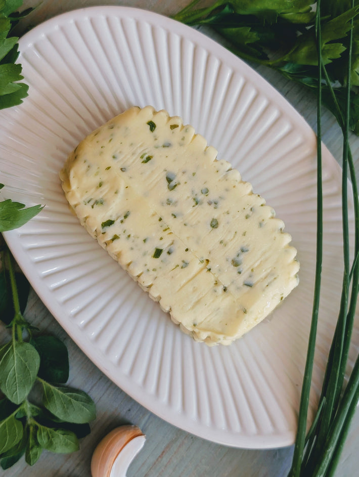 Compound herb butter with chives and parsley on a white ridged serving plate, garlic clove and herbs beside it.