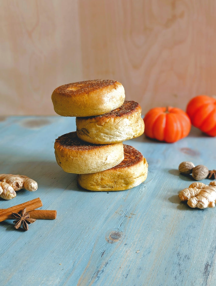 Stack of four toasted English muffins on a blue wooden table with small pumpkins and spices nearby