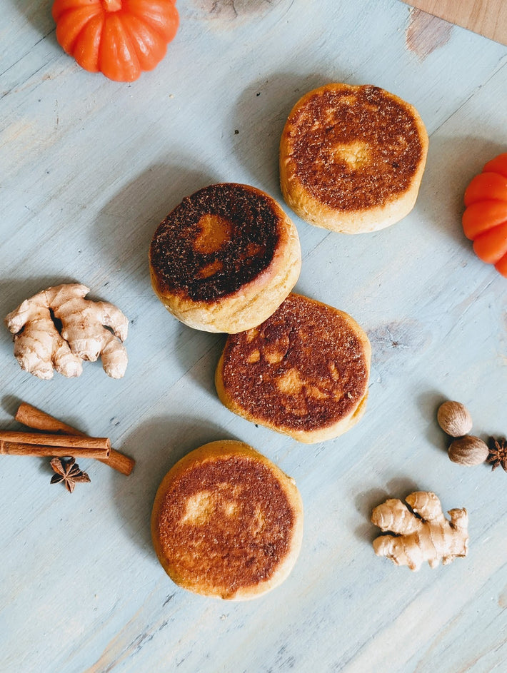 Four toasted English muffins on blue wooden board with ginger, cinnamon sticks, star anise, nutmeg and small pumpkins
