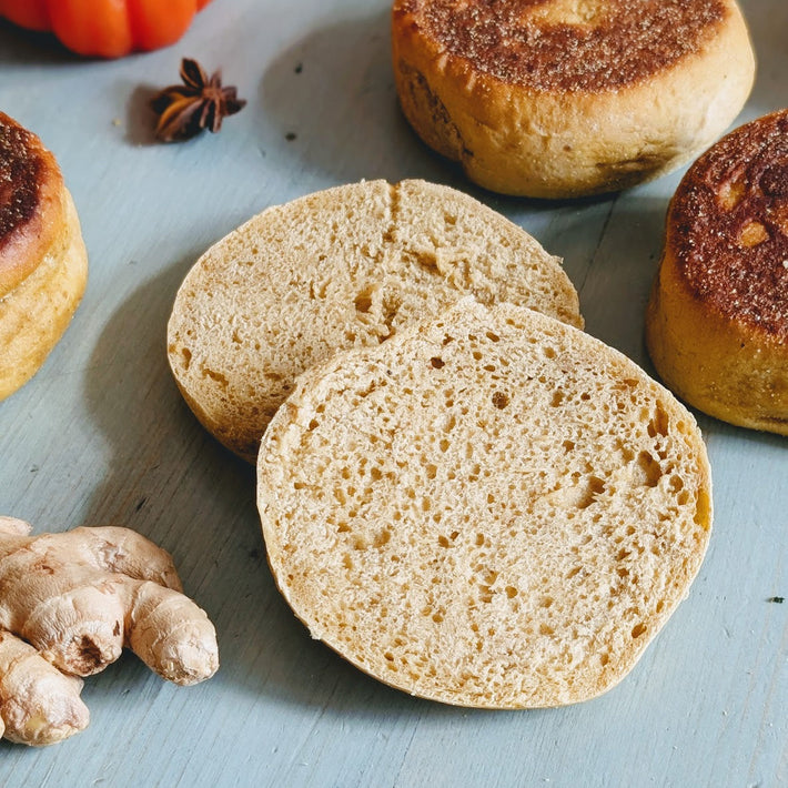 Two halved English muffins on a blue board, with whole toasted muffins, fresh ginger root and a star anise.