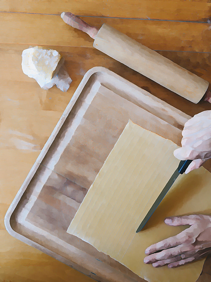 A person cutting pasta dough with a knife on a wooden surface