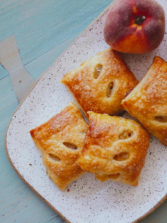 Four golden-brown Peach Pie Bites on a plate with a peach on the side