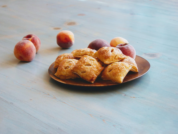 A plate of Wildgrain Peach Pie Bites with fresh peaches on the side