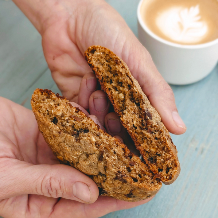 Close-up of Protein Breakfast Cookie Oatmeal Raisin split in half showing chewy oats and raisins, hands holding