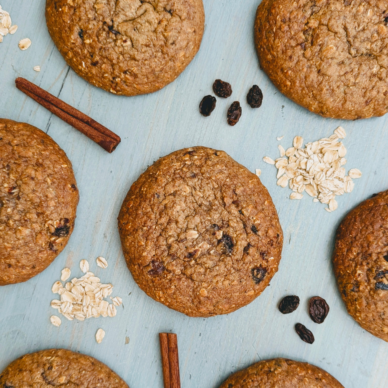 Top-down view of Protein Breakfast Cookie Oatmeal Raisin showing oatmeal texture, raisins and cinnamon on pale blue board