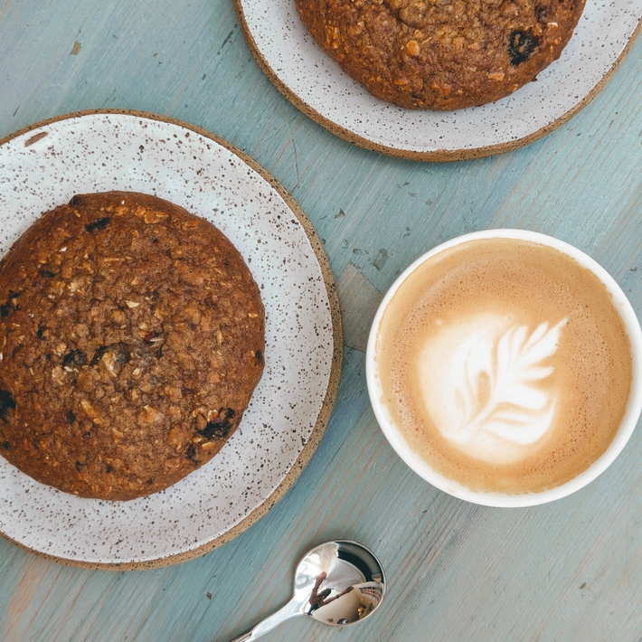 Top-down view of Protein Breakfast Cookie - Oatmeal Raisin showcasing oatmeal texture and raisins with a latte on a blue wooden table