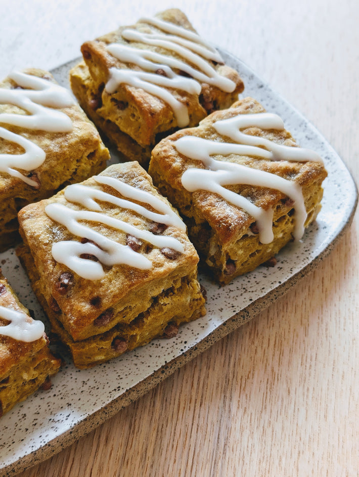 Pumpkin Cinnamon Biscuits on a plate, golden-brown with white icing and chocolate chips.
