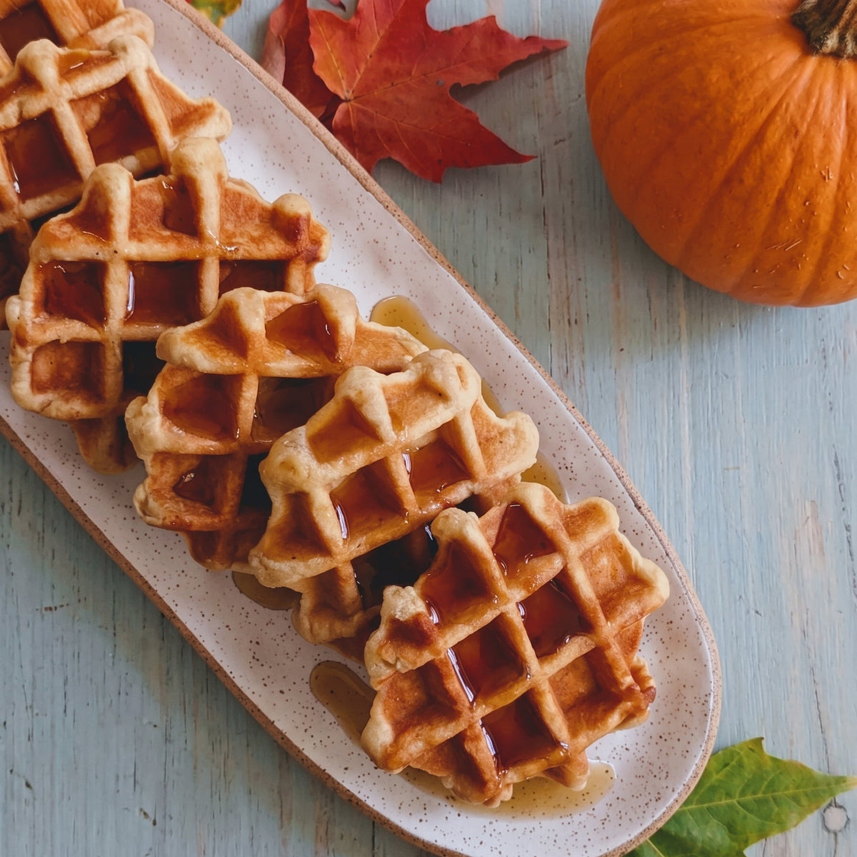 Overhead view of pumpkin spice Belgian waffles drizzled with syrup on a platter with pumpkins and autumn leaves