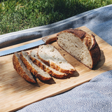 Top view of Sourdough Rosemary Garlic Loaf sliced to show airy crumb and golden crust on wooden board with picnic blanket