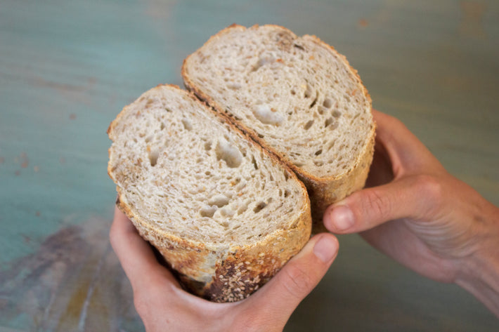 A person holding a sliced sourdough sesame seed loaf, showcasing its texture.