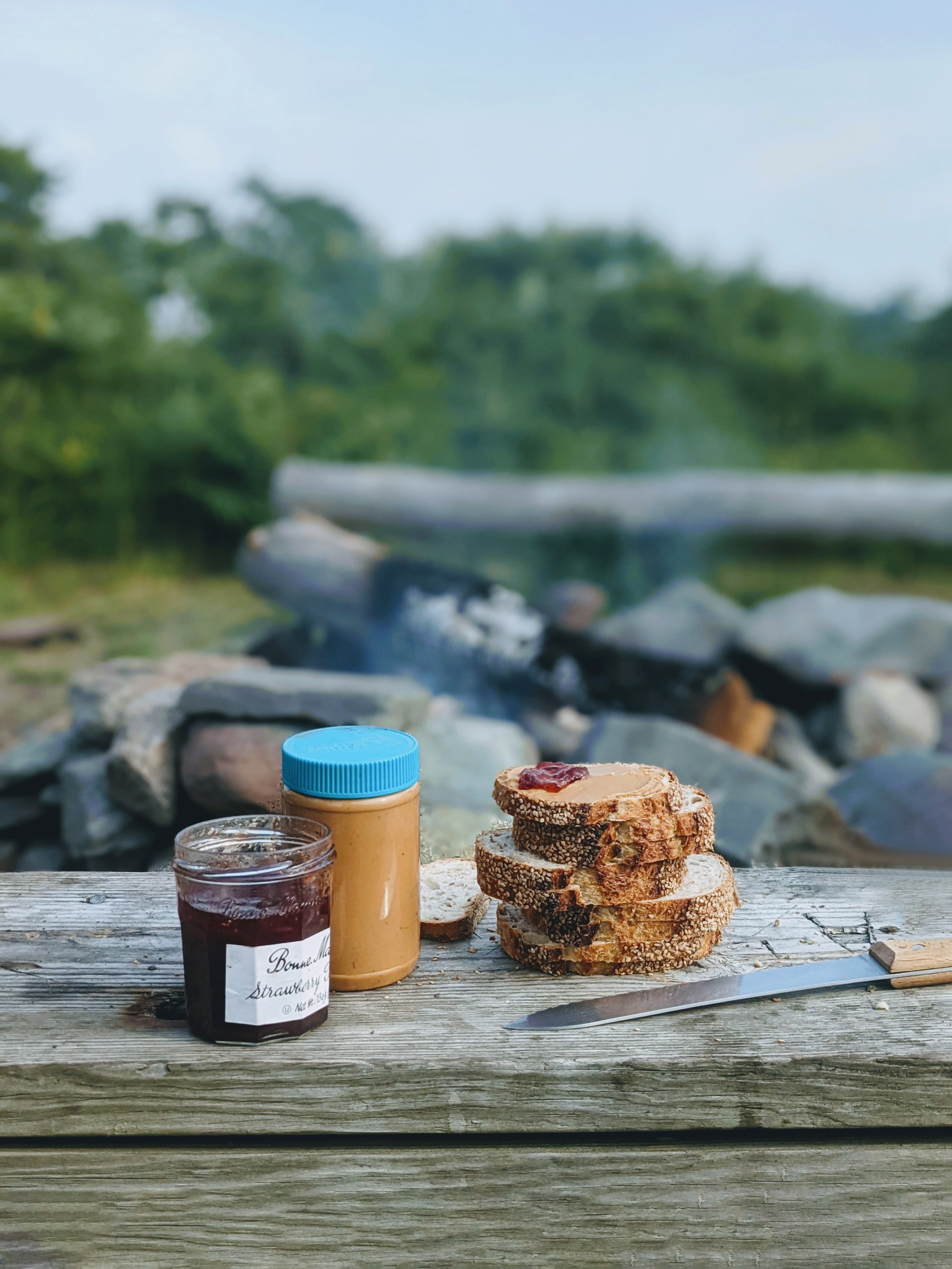 Sourdough sesame seed loaf with peanut butter and jam on a wooden table outdoors