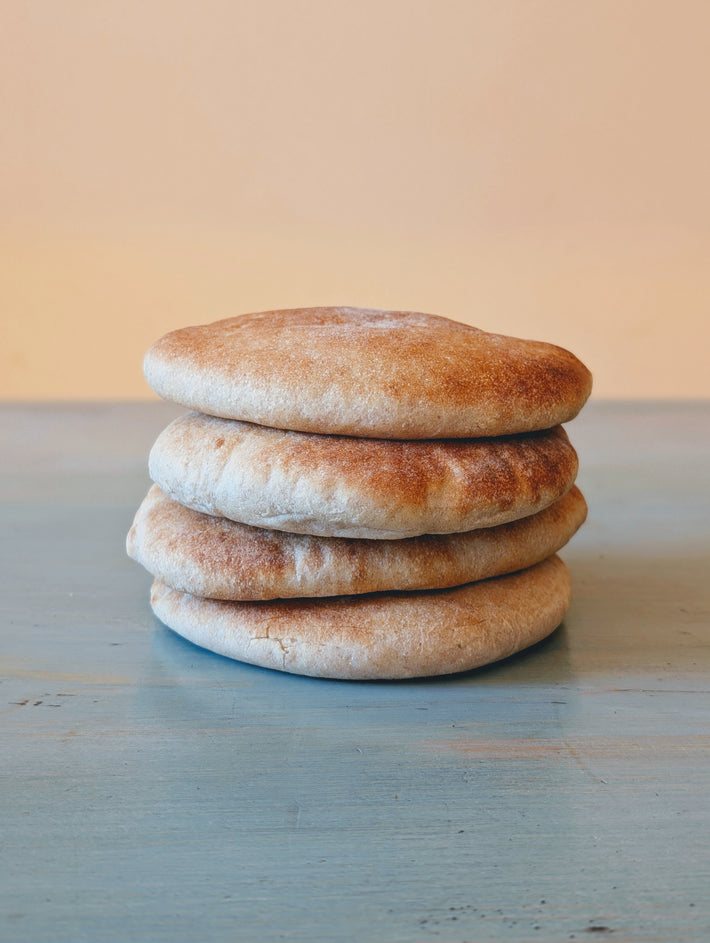 Slow-Fermented Artisanal Pita (4-pack) stacked on a wooden surface.