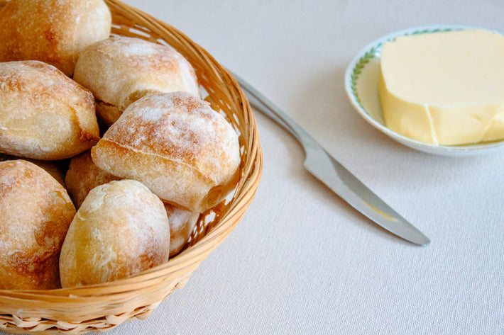 A basket of crusty sourdough rolls next to a butter dish and knife.