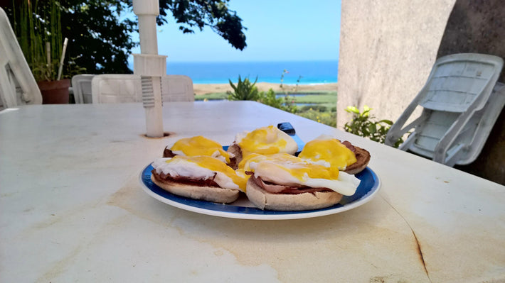 Plate of English muffins topped with poached eggs and hollandaise sauce on a table with a seaside view.