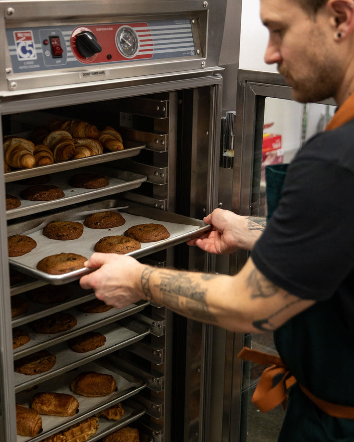 Person removing trays of baked goods from a large industrial oven.