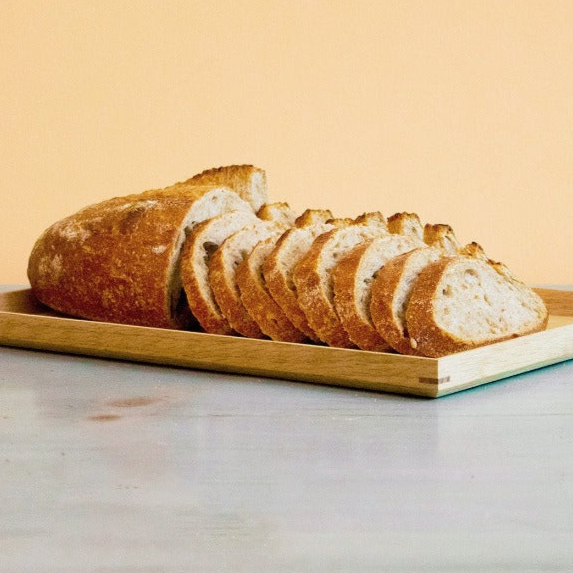 Sliced sourdough whole wheat loaf on a wooden board against a peach background
