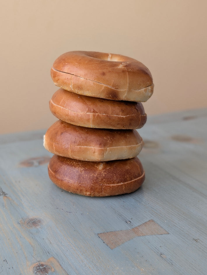 Four plain bagels stacked on a weathered blue wooden table with a beige background.