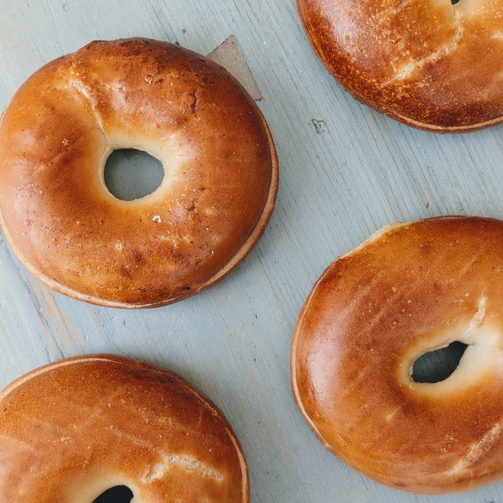 Four plain golden bagels arranged on a light-blue wooden board