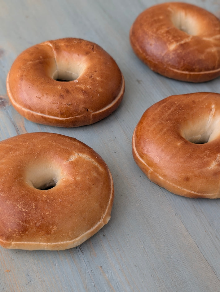 Four plain bagels on a worn blue wooden surface