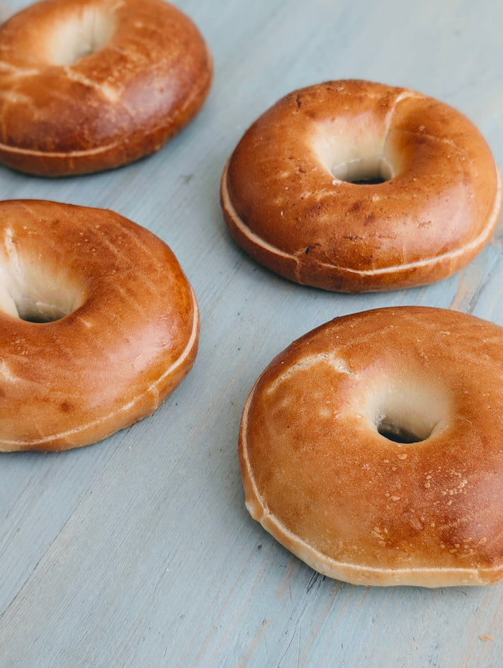 Four plain bagels with golden-brown crusts arranged on a pale blue wooden surface