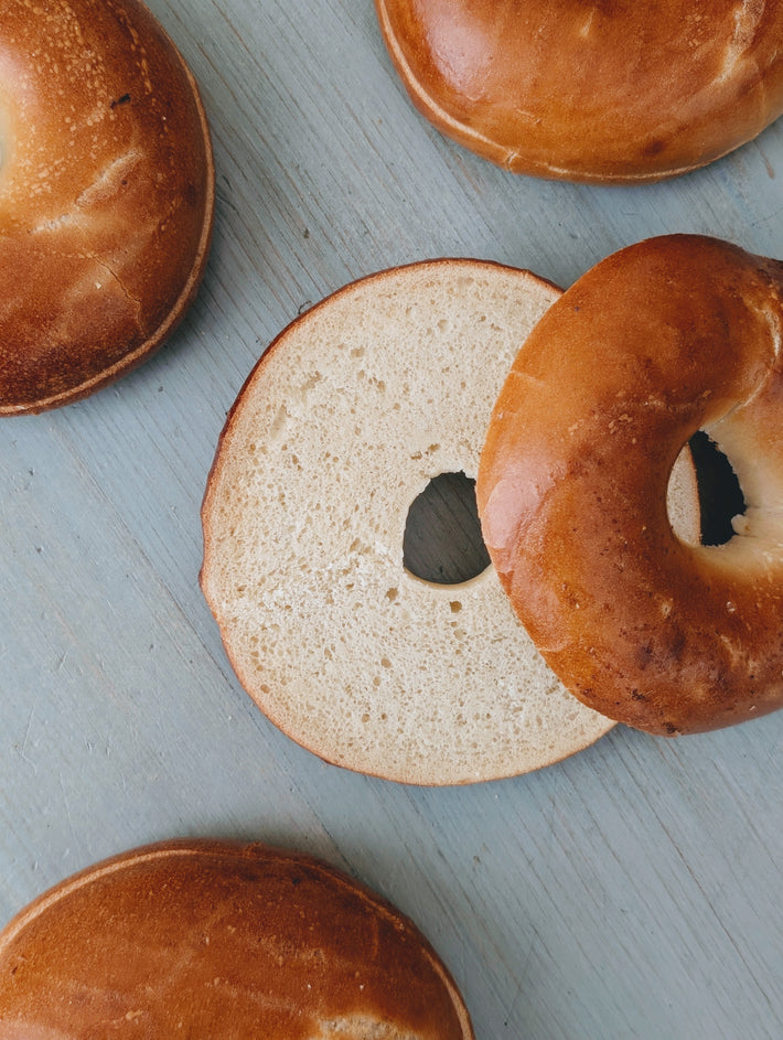 Plain bagels on a blue wooden surface, one sliced open to show the interior crumb