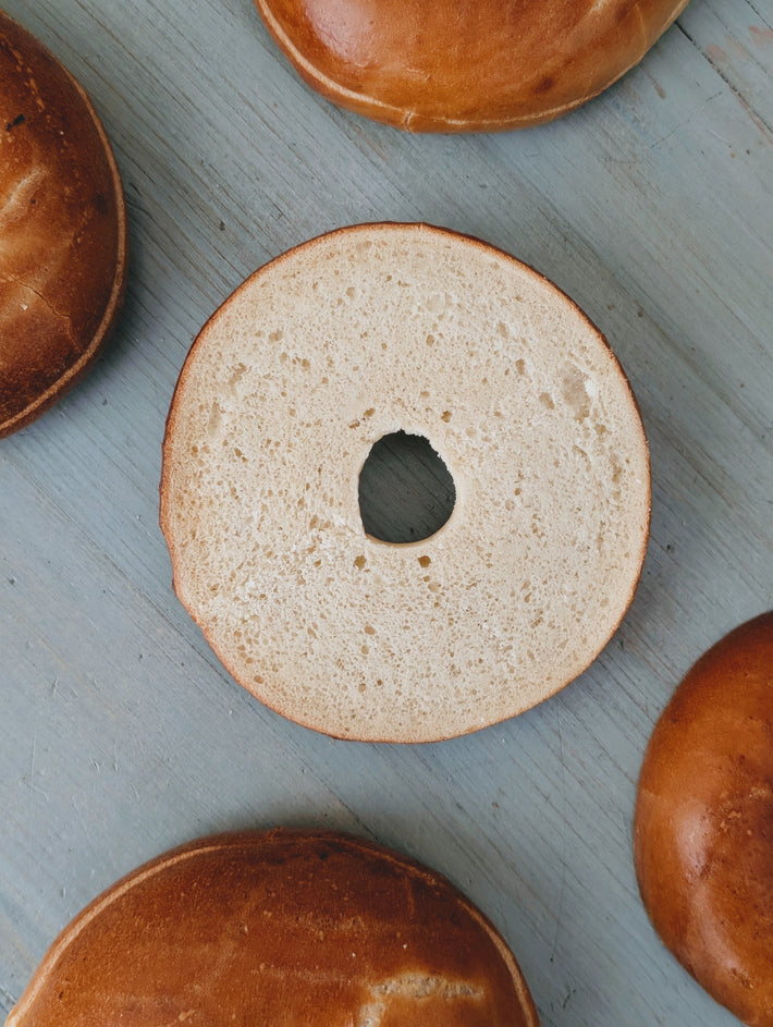 Sliced plain bagel half on a blue wooden board, surrounded by whole plain bagels