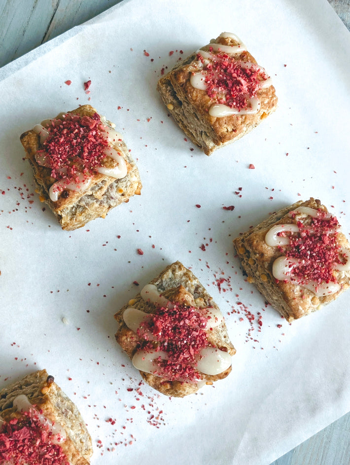 Overhead of strawberry white chocolate biscuits, flaky squares drizzled and topped with crushed strawberries on parchment