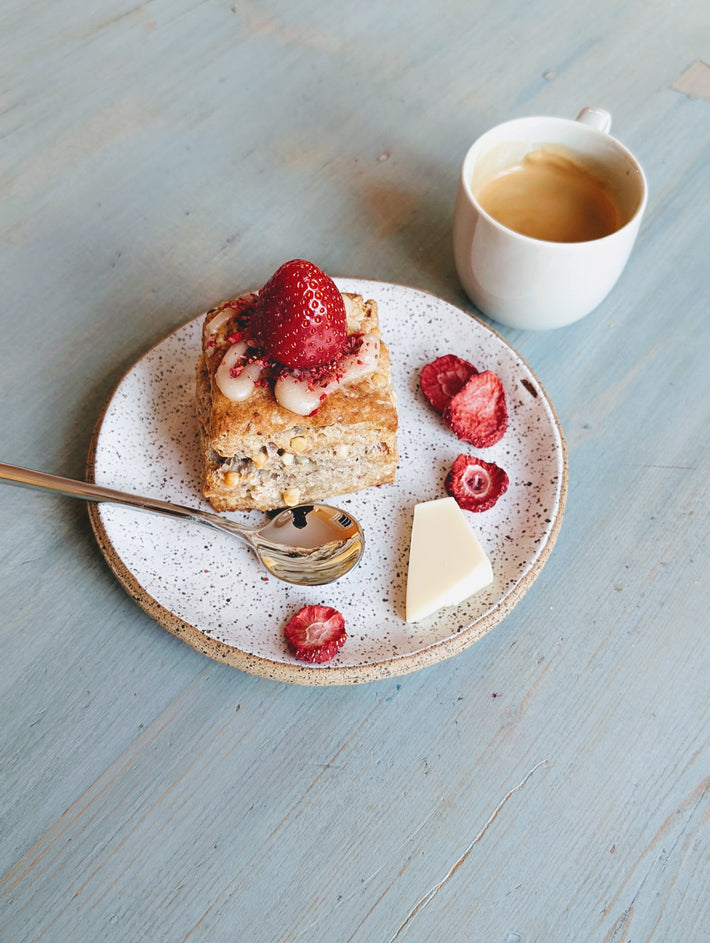 Top-down view of strawberry white chocolate biscuit topped with fresh strawberry on speckled plate with espresso