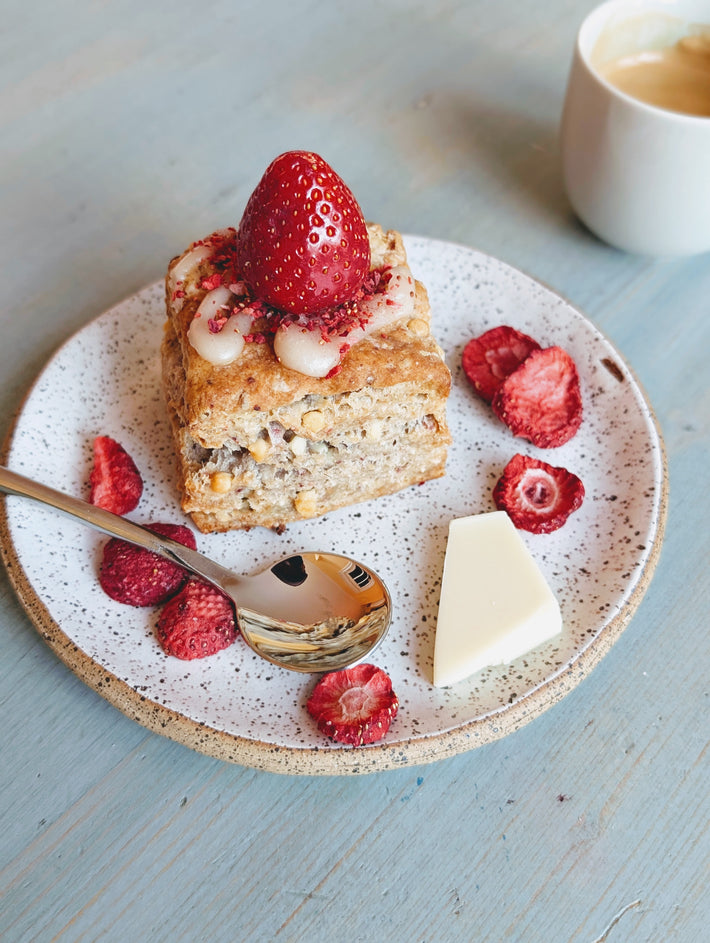 Angled view of Strawberry White Chocolate biscuit with white chocolate drizzle, whole strawberry, dried berries on plate