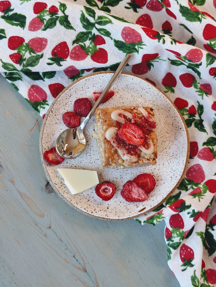 Top view of a strawberry white chocolate biscuit with white chocolate drizzle and dried strawberry pieces on a speckled plate