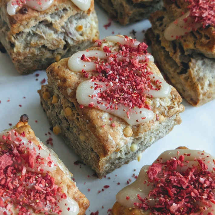 Three-quarter close-up of strawberry white chocolate biscuits with white chocolate glaze and crushed freeze-dried strawberries on parchment