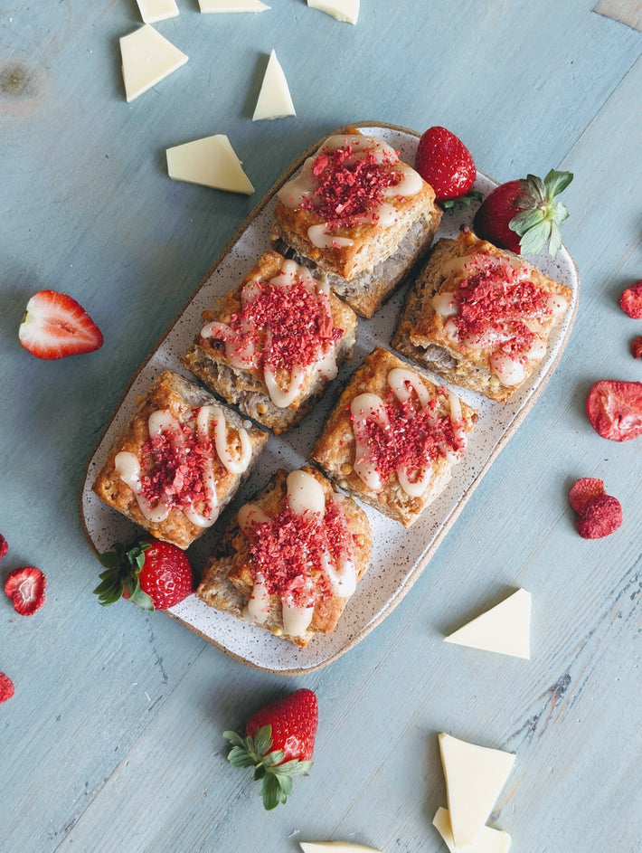 Six strawberry white chocolate biscuits on a plate, drizzled with white chocolate and sprinkled with freeze dried strawberry