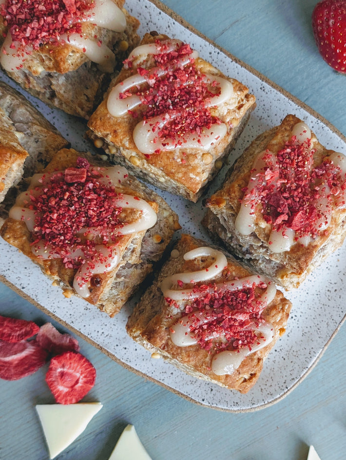 Top-down of six strawberry white chocolate biscuits with white chocolate drizzle and crushed strawberries on speckled plate