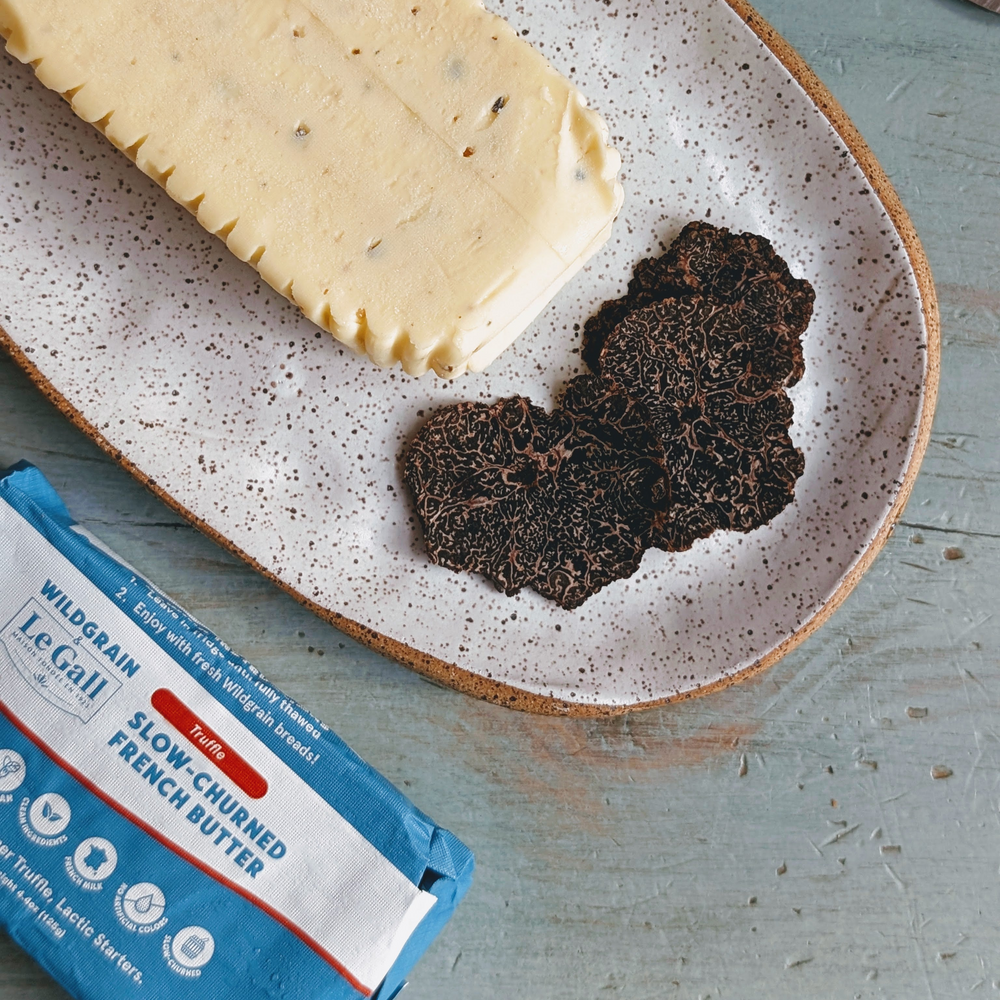 Truffle butter block and sliced truffle on speckled plate; package: WILDGRAIN Le Gall Truffle SLOW-CHURNED FRENCH BUTTER