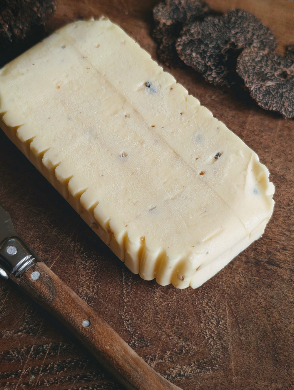 Block of truffle butter with visible truffle flecks on a wooden cutting board beside a wooden-handled butter knife