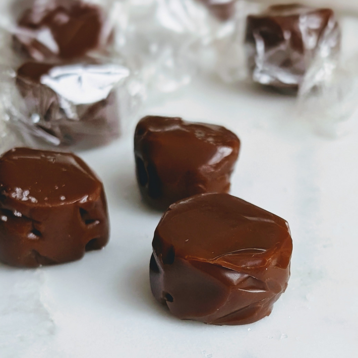 Soft brown caramels, two unwrapped on parchment and two wrapped in translucent wax paper