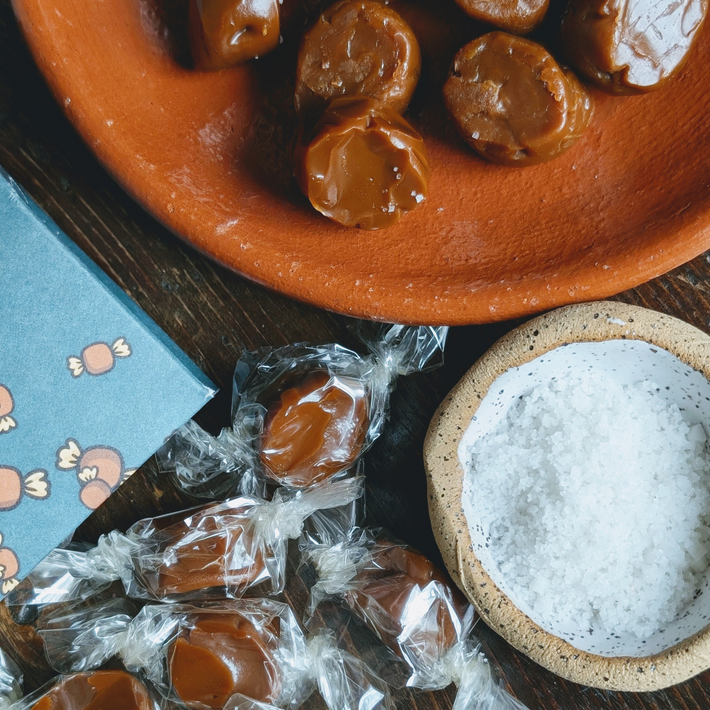 Salted caramels: cellophane-wrapped caramels on wood, unwrapped caramels on a terracotta plate, and a bowl of coarse salt
