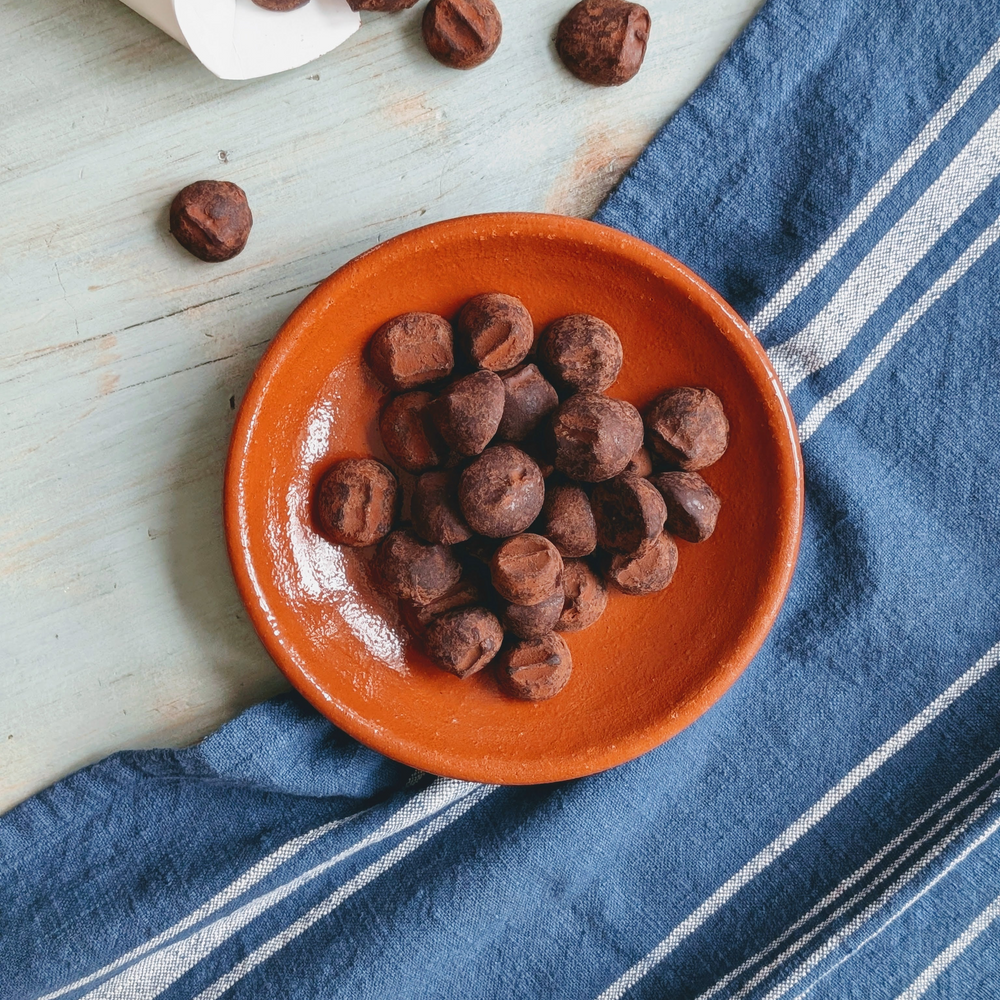 Chocolate truffles in an orange bowl on a blue striped towel with a package in the background.